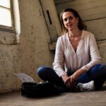 Die Lektorin Christine Storck sitzt im Schneidersitz vor einer Schreibmaschine