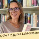 Lektorin Christine Storck steht mit einem Buch im Arm vor ihrem Bücherregal und lächelt in die Kamera.