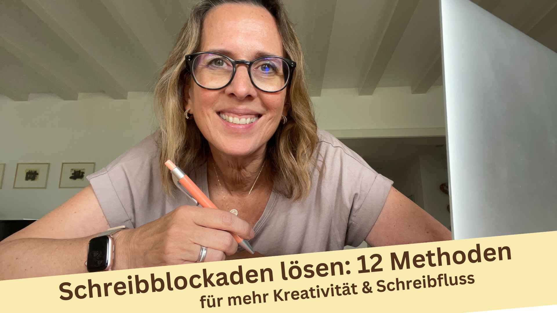 Lektorin Christine Storck sitzt mit Stift in der Hand vor ihrem Schreibtisch und lächelt in die Kamera und denkt an 12 bewährte Methoden, um Schreibblockaden aufzulösen