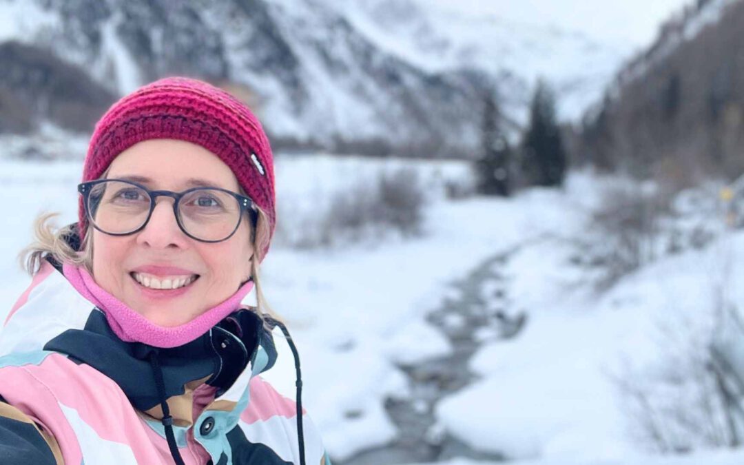 Lektorin Christine Storck lacht bei einem Schneespaziergang in Sulden/Südtirol in die Kamera.