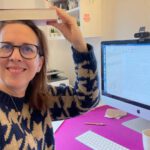 Lektorin Christine Storck sitzt in ihrem Büro am Schreibtisch und jongliert ein Buch auf ihrem Kopf