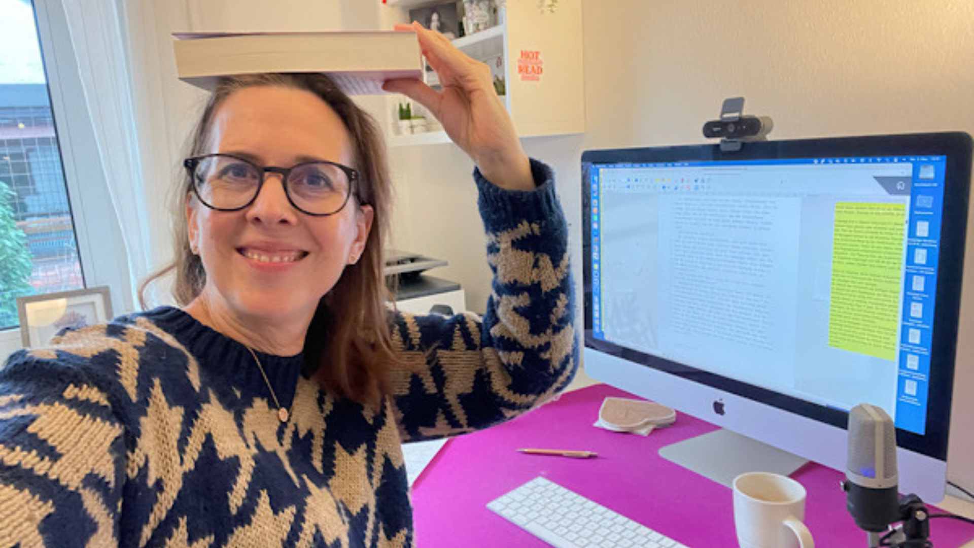 Lektorin Christine Storck sitzt in ihrem Büro am Schreibtisch und jongliert ein Buch auf ihrem Kopf