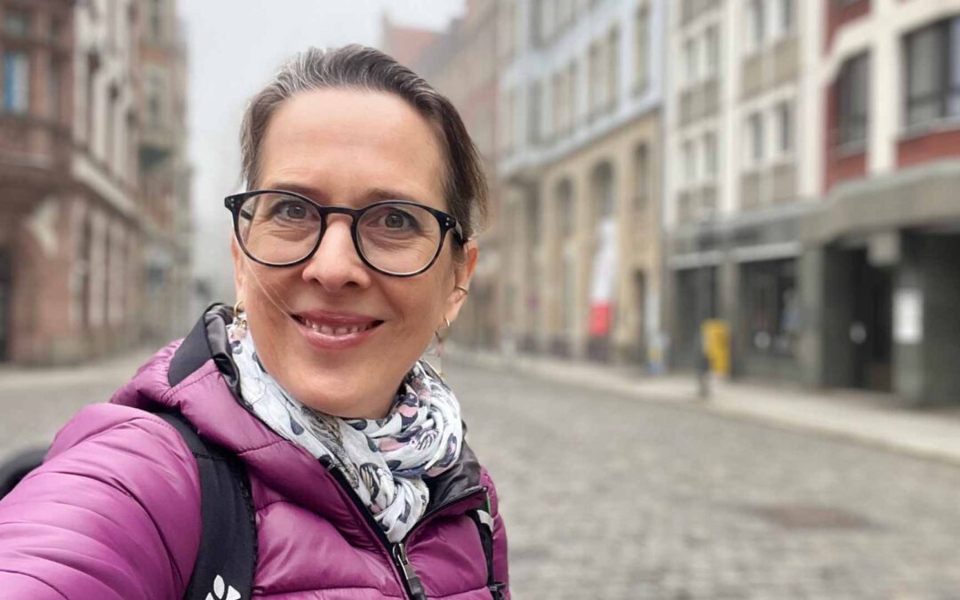 Lektorin Christine Storck steht morgens in der Leipziger Altstadt und lacht in die Kamera