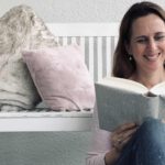 Lektorin und Autorin Christine Storck sitzt vor einer Bank und liest lachend ein Buch.