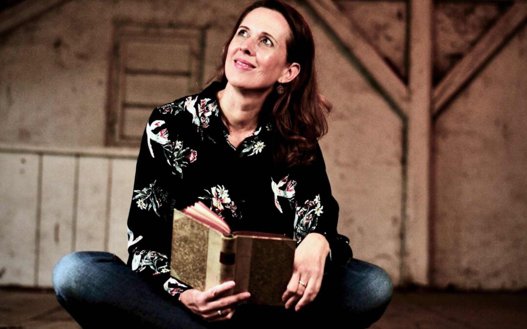 Lektorin und Romanautorin Christine Storck sitzt mit einem Buch lächelnd auf einem alten Dachboden