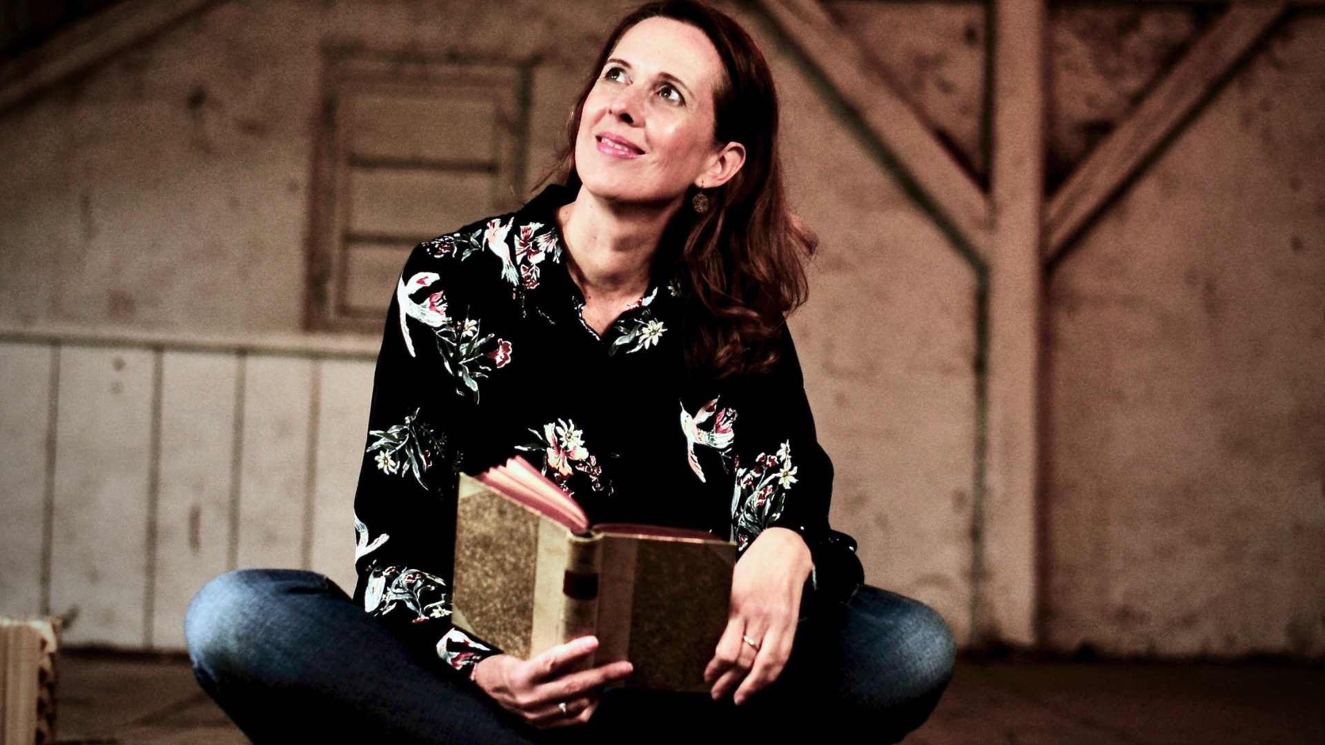 Lektorin und Romanautorin Christine Storck sitzt mit einem Buch lächelnd auf einem alten Dachboden